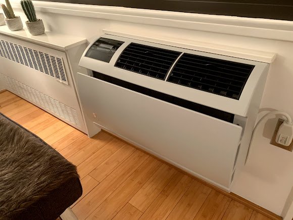 Console-style indoor air conditioning unit mounted near the floor, providing heating and cooling in a modern living space