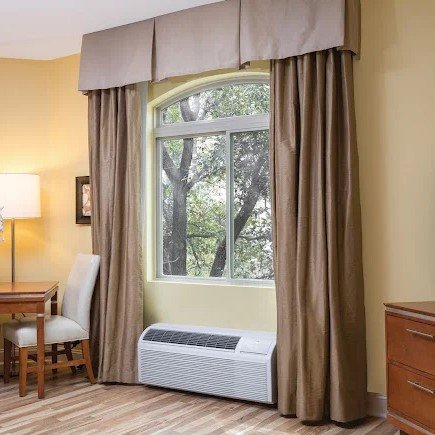 A PTAC unit installed below a window in a living area.